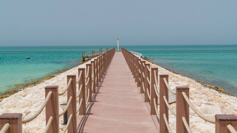 A wooden pier extending into a turquoise sea with clear skies.