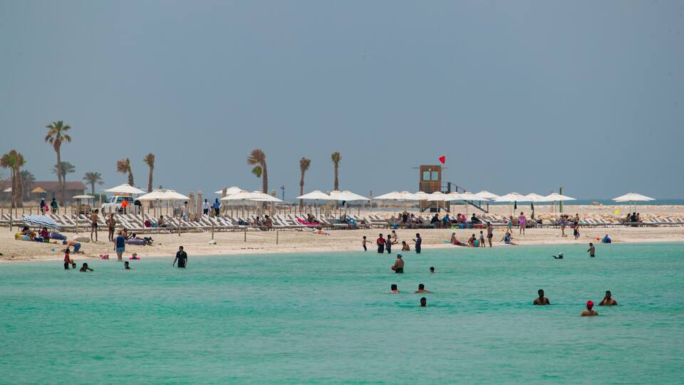 A crowded beach with people swimming and sunbathing under umbrellas.