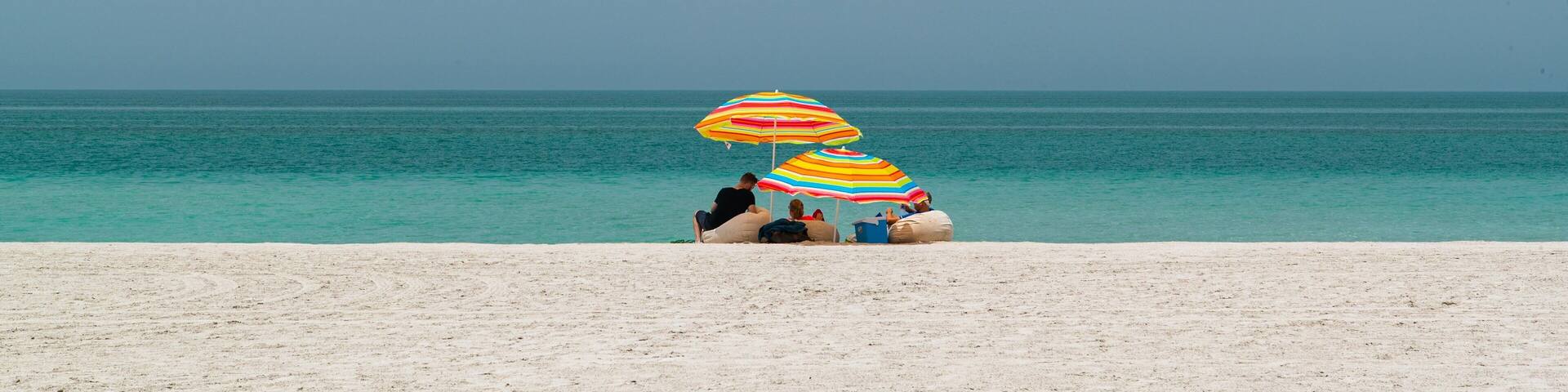 A beach with two colorful umbrellas and people relaxing on the sand.