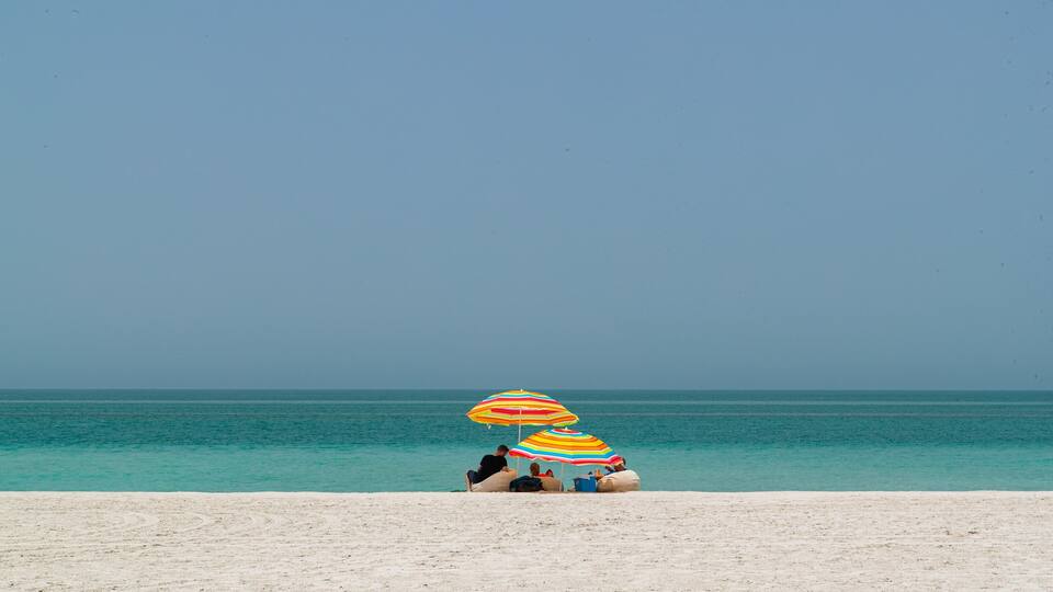 A beach with two colorful umbrellas and people relaxing on the sand.