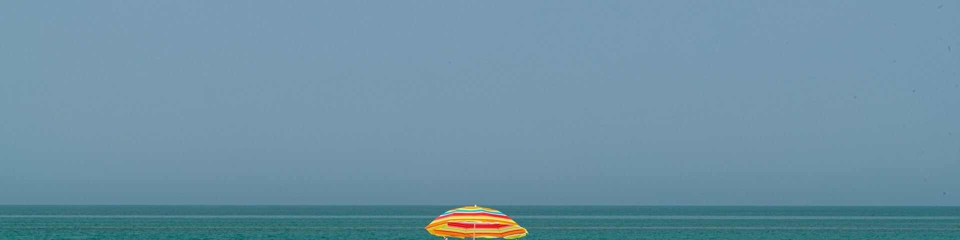 Una playa con dos sombrillas coloridas y gente descansando en la arena.