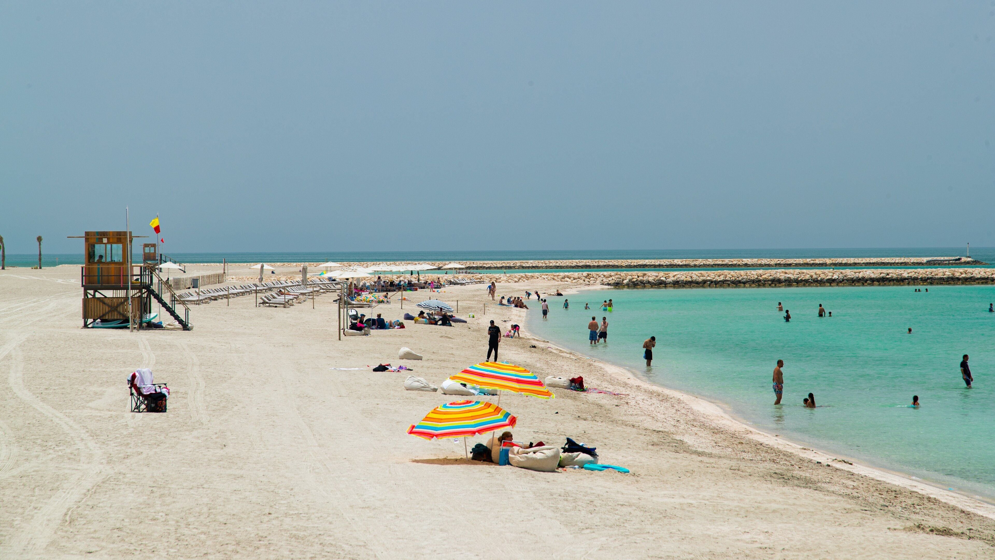 A sandy beach with a lifeguard tower, umbrellas, and people swimming and relaxing.