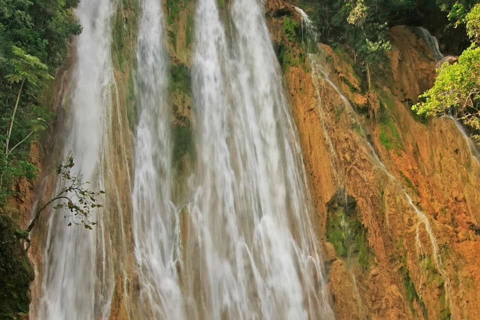 A waterfall cascading down a rocky cliff surrounded by lush greenery.