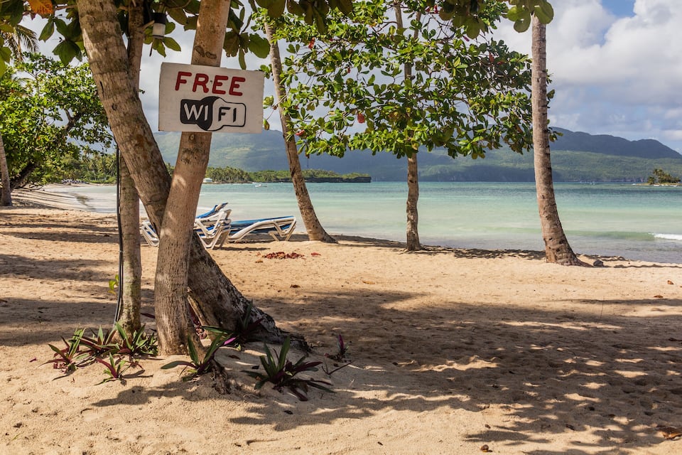 A beach with a 'FREE WiFi' sign, palm trees, and a boat in the background.