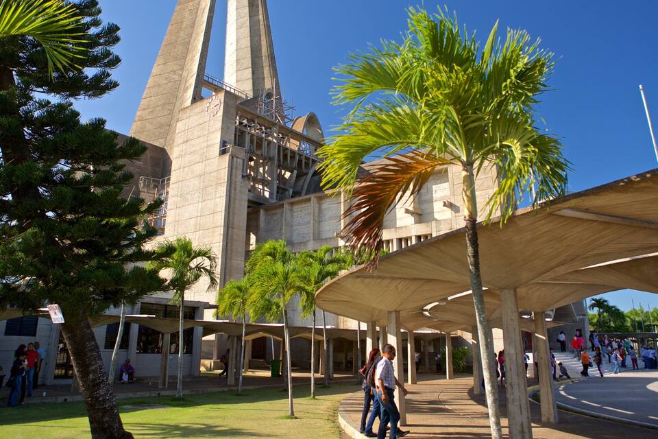 Un edificio moderno con una torre de reloj, rodeado de palmeras y gente.