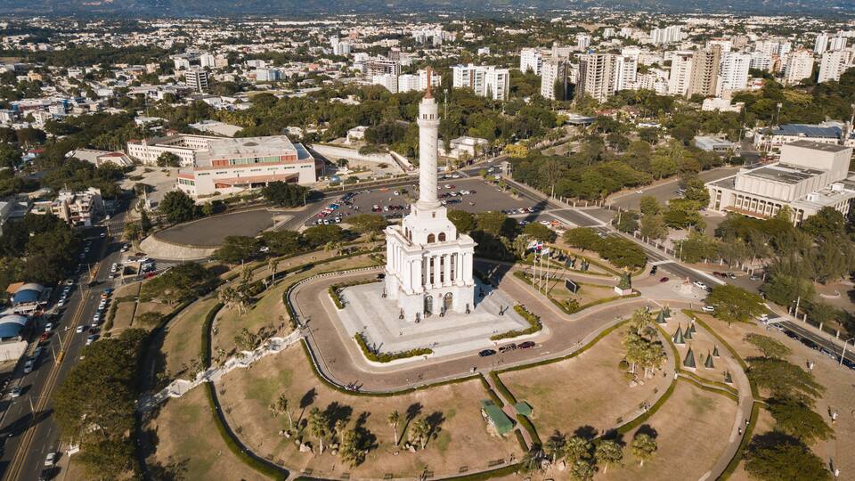 A cityscape with a prominent white monument surrounded by a landscaped park, amidst residential and commercial buildings.