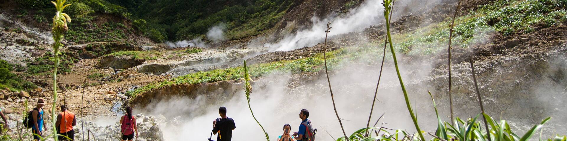 A mountainous landscape with a steam vent, hikers, and lush greenery.