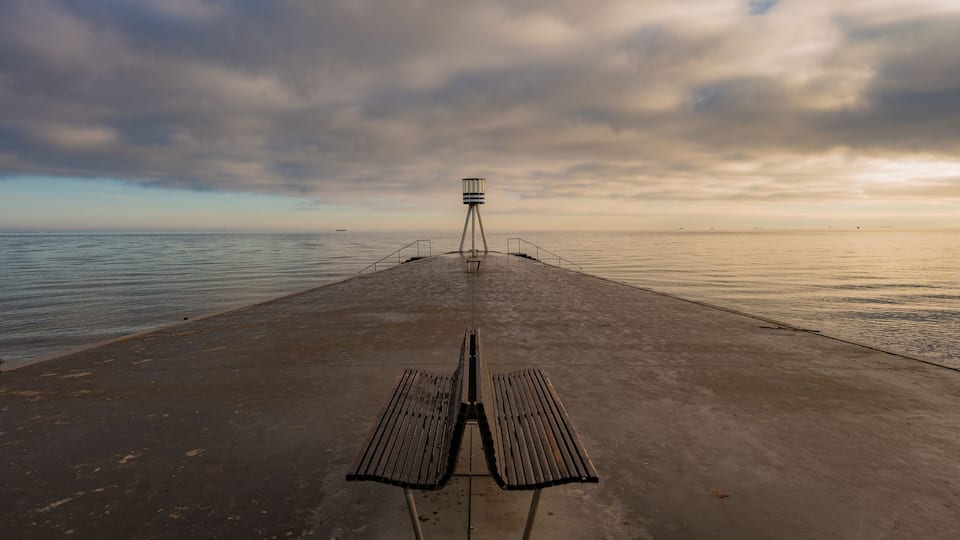 A concrete pier with a bench and a lighthouse in the distance.