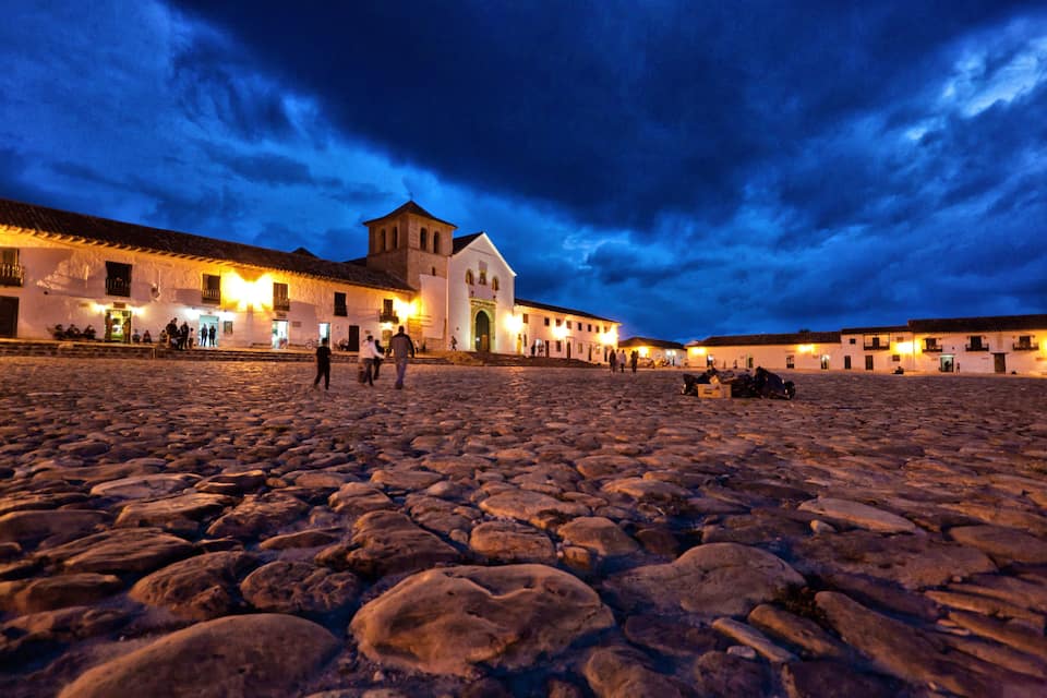 A historic stone square with buildings and a church at twilight.