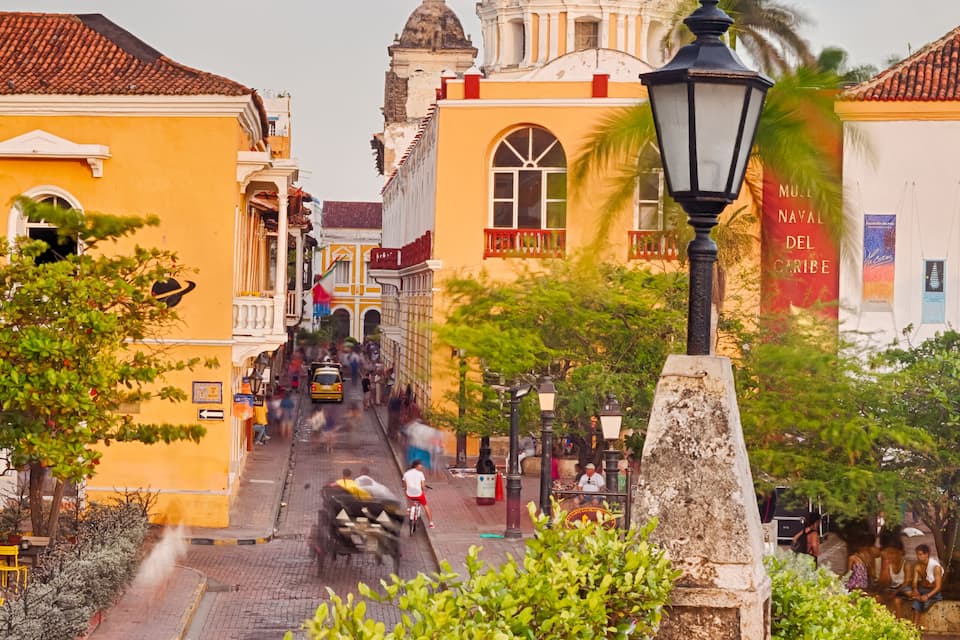Una calle histórica con una iglesia destacada, camino de adoquines y abundante vegetación.