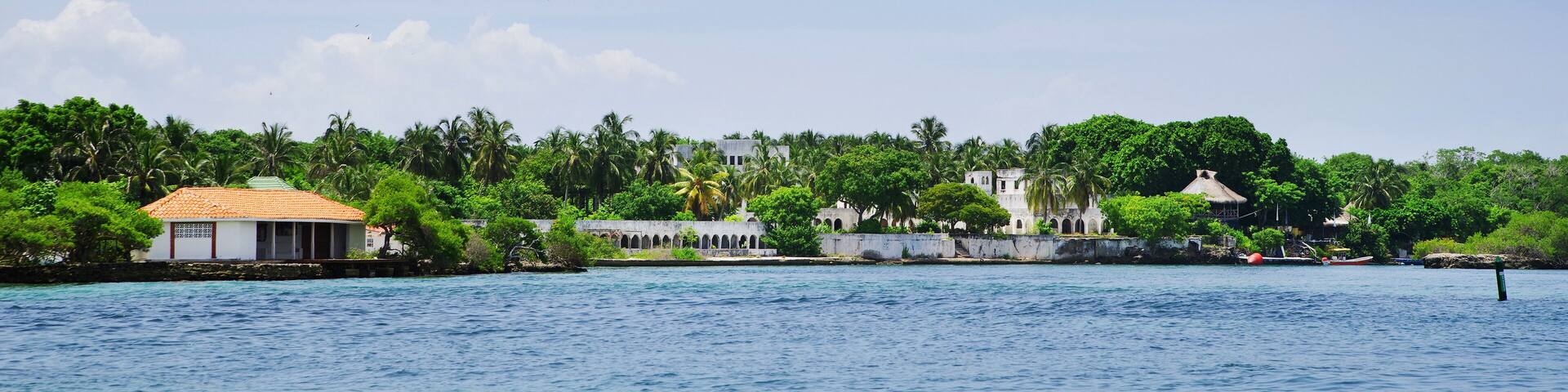 A coastal town with a white building with a red roof, surrounded by lush greenery and palm trees.