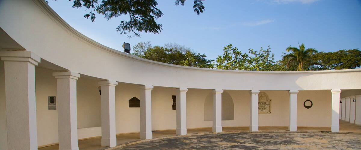 A courtyard with white columns, a stone floor, and trees in the background.