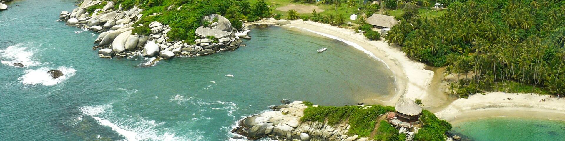 Una playa tropical con aguas turquesas cristalinas, afloramientos rocosos y densa selva verde.