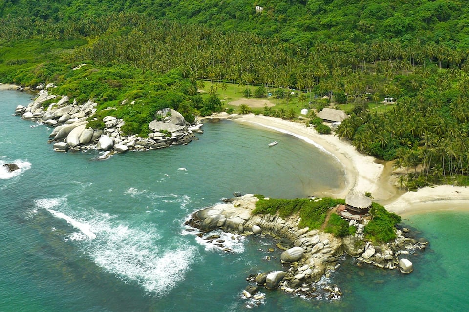 Ein tropischer Strand mit klarem türkisblauem Wasser, felsigen Landzungen und dichtem Grünland.