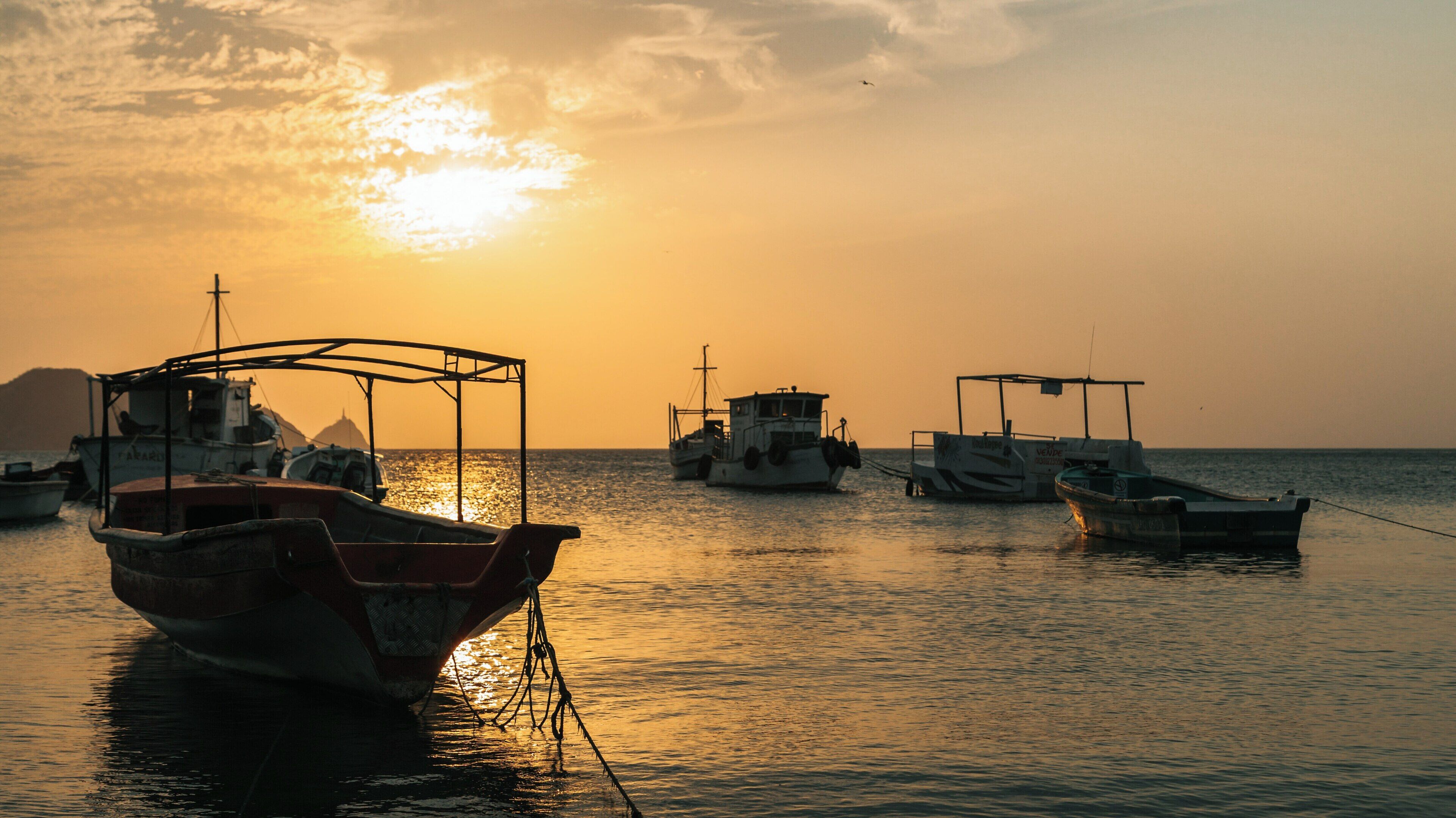 Sunset casts a warm glow over Taganga Beach in Santa Marta, Magdalena, Colombia with fishing boats gently bobbing in the water