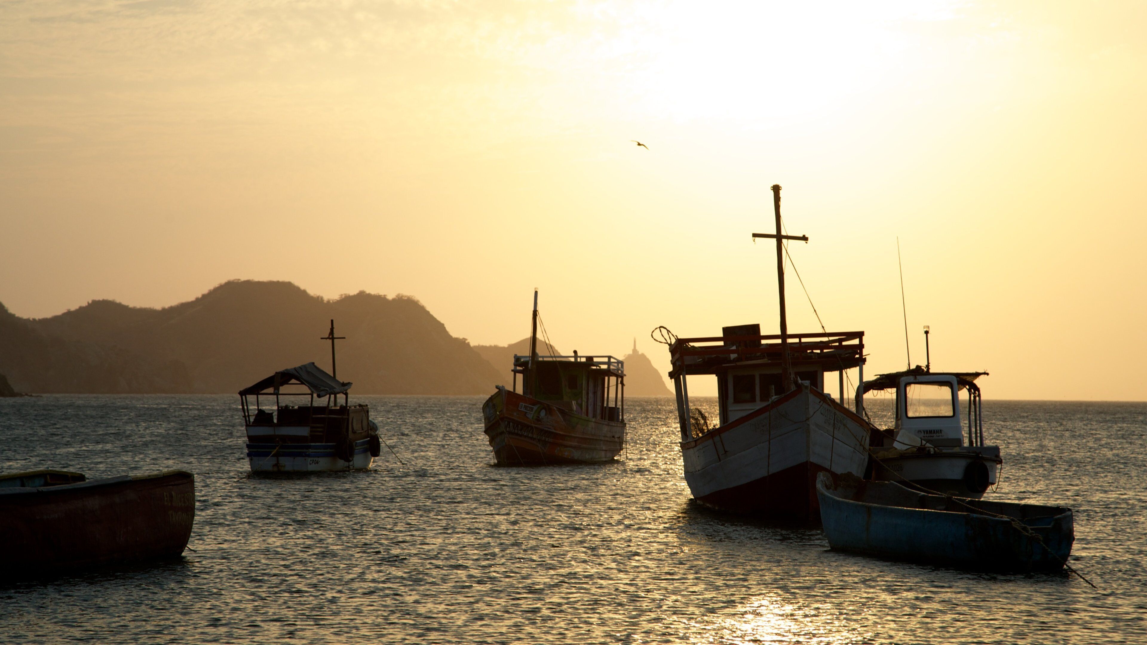 A sunset over a calm sea with several fishing boats anchored.