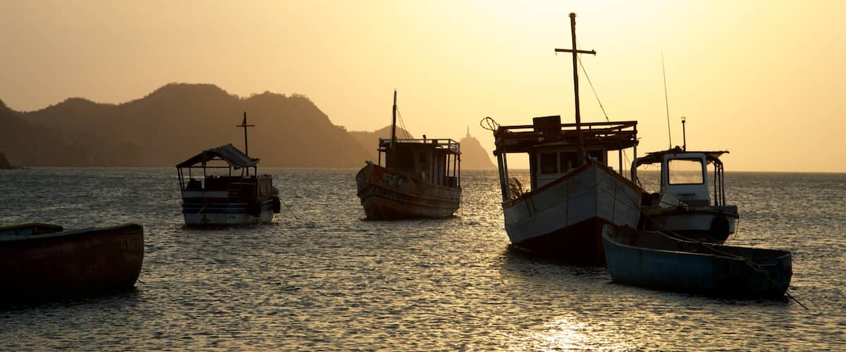 A sunset over a calm sea with several fishing boats anchored.