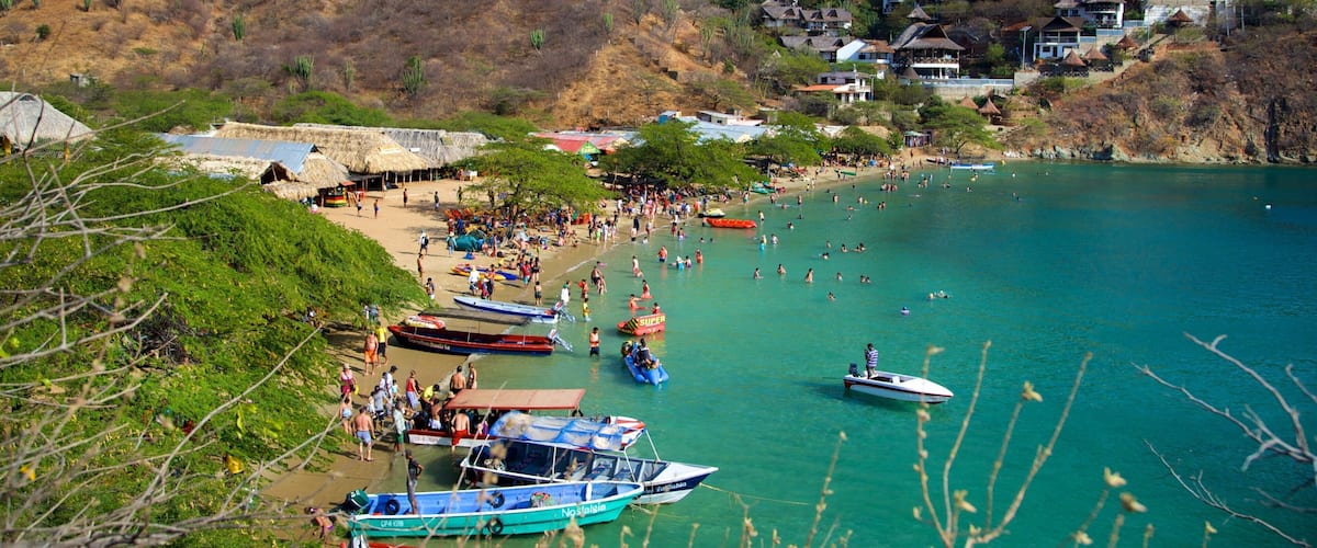 A coastal village with thatched-roof houses, a beach, and clear turquoise waters.