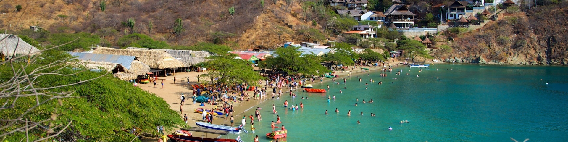 A coastal village with thatched-roof houses, a beach, and clear turquoise waters.