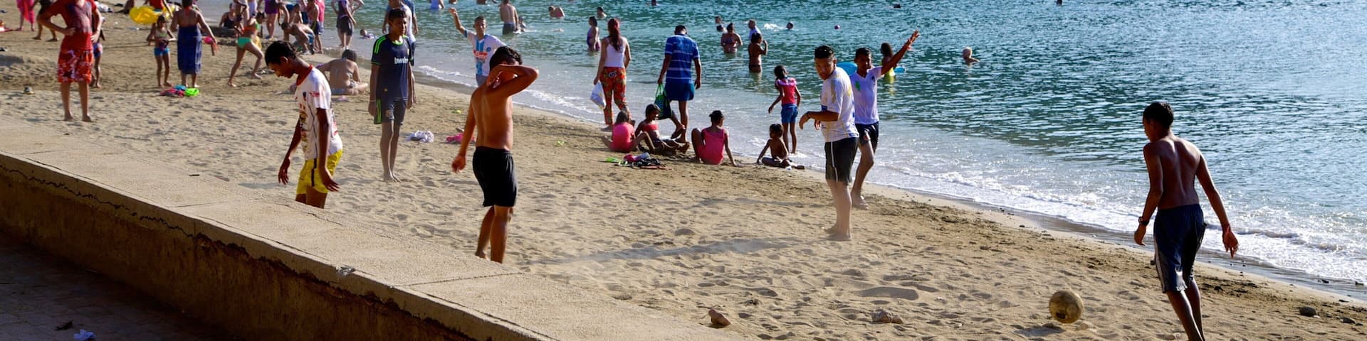A crowded beach with people swimming and walking along the shore.