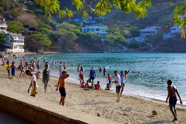 Uma praia movimentada com pessoas nadando e caminhando pela orla.
