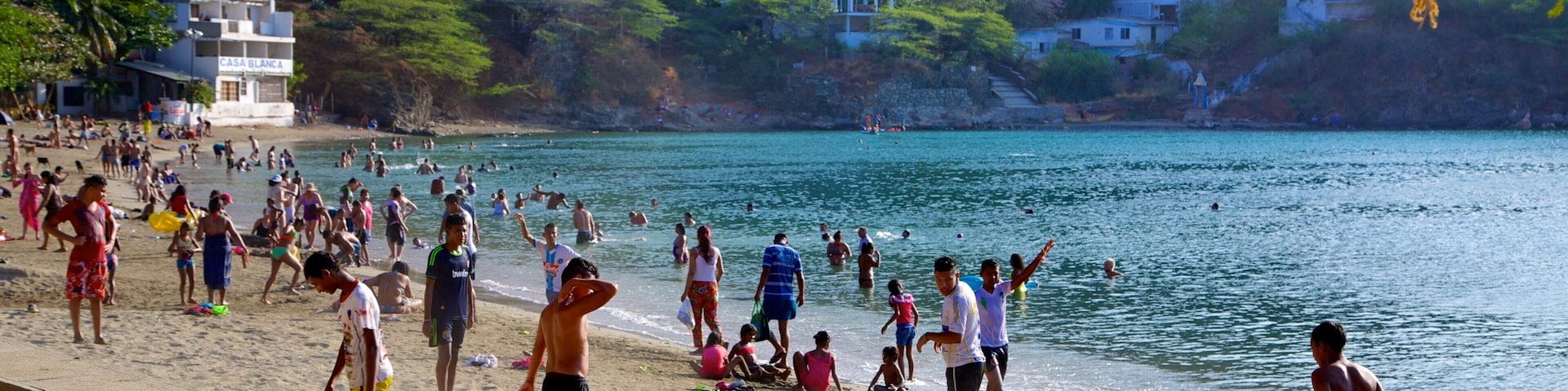 Uma praia movimentada com pessoas nadando e caminhando pela orla.