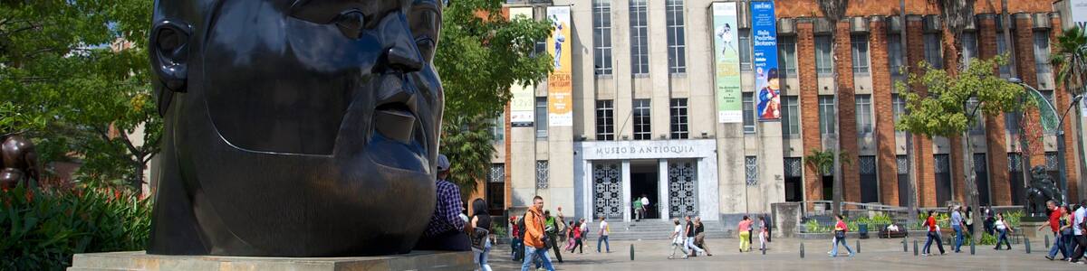 A large sculpture of a man's face in a public square with palm trees and a museum in the background.