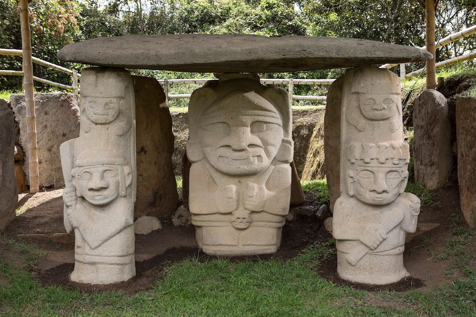 A stone structure with three pillars, each featuring a carved face, and a flat stone roof supported by the pillars.