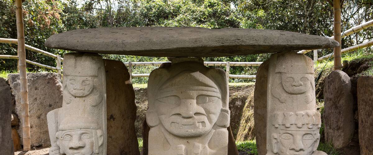 A stone structure with three pillars, each featuring a carved face, and a flat stone roof supported by the pillars.