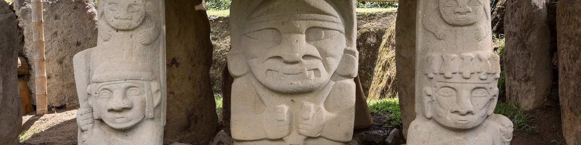 A stone structure with three pillars, each featuring a carved face, and a flat stone roof supported by the pillars.