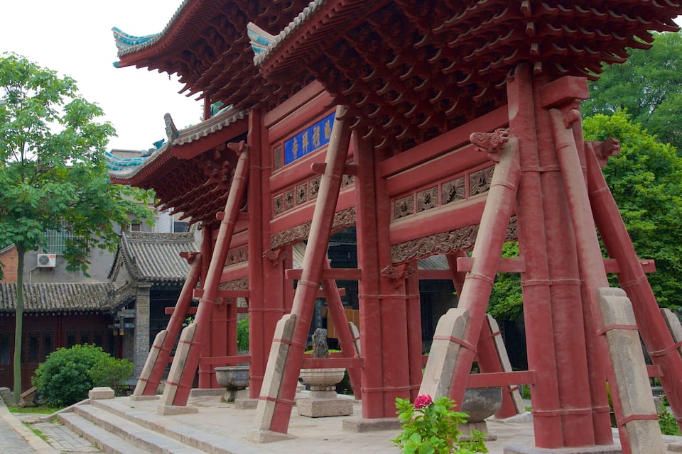 A traditional red Chinese pavilion with intricate carvings and a blue sign.