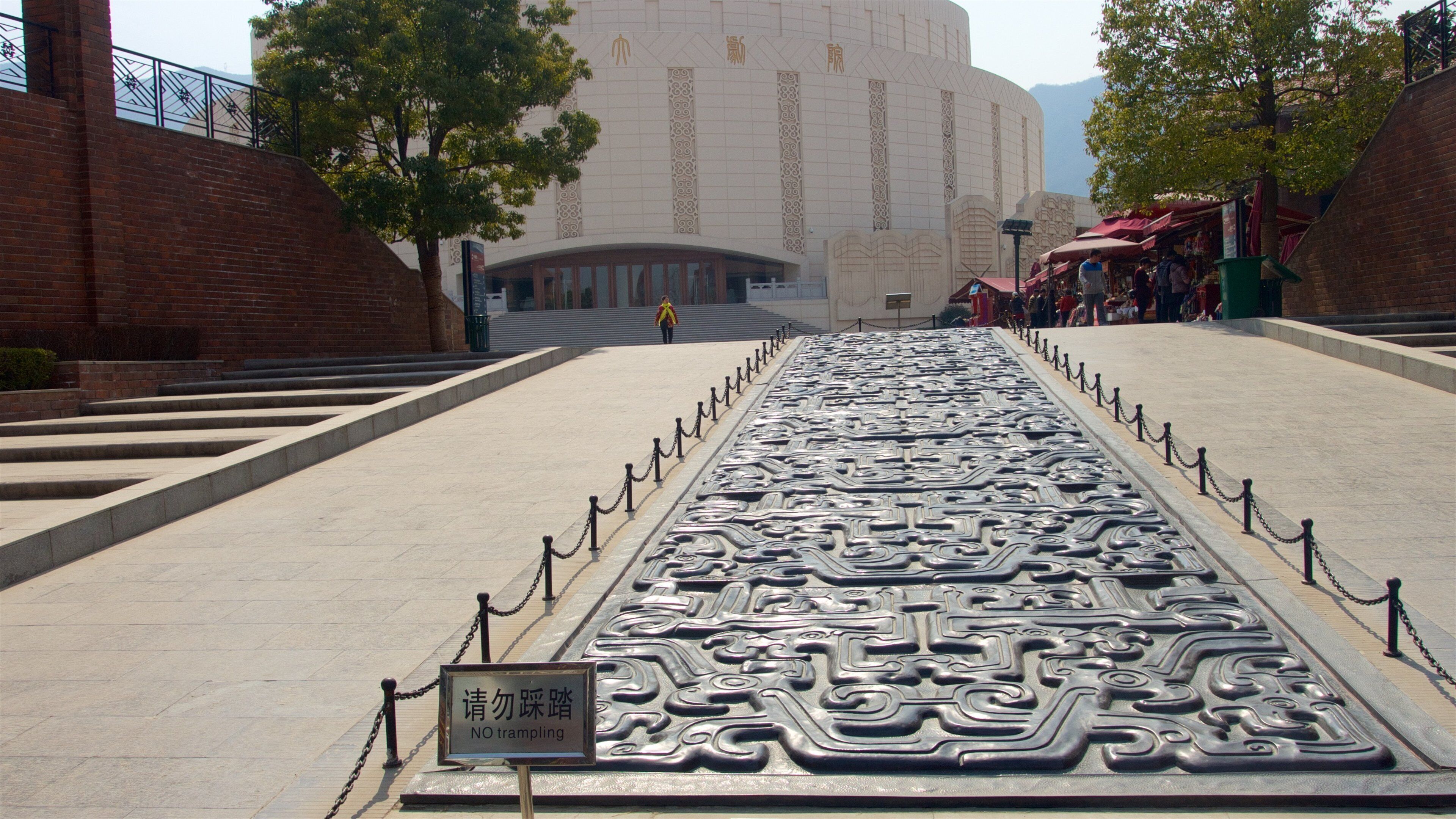 A large, ornate metal sculpture with intricate designs, surrounded by a paved walkway and a sign that reads "NO tramping."