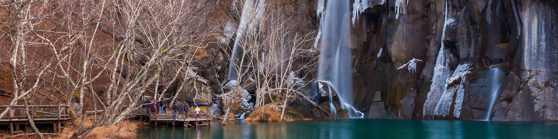 A waterfall cascading into a turquoise lake surrounded by leafless trees and rocky cliffs.