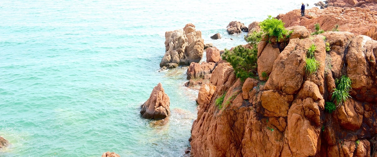 A rocky coastline with clear turquoise water and a person standing on a rock.