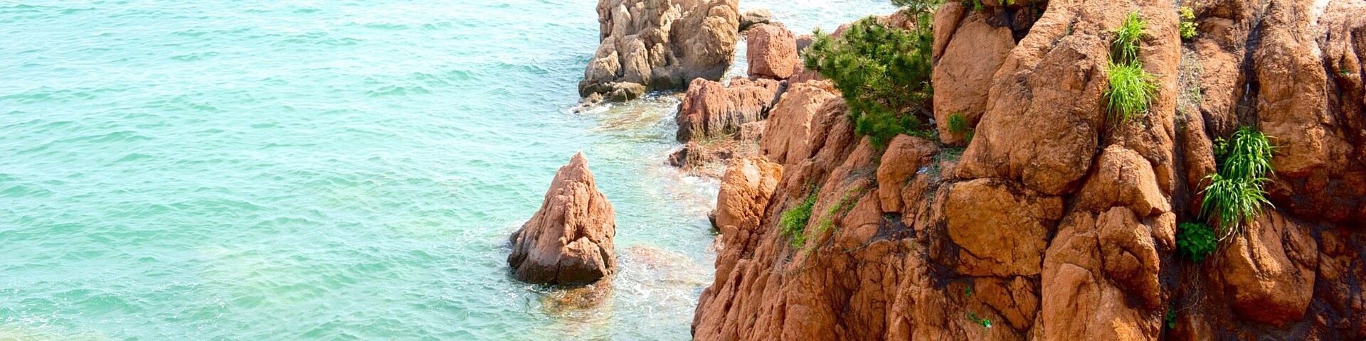 A rocky coastline with clear turquoise water and a person standing on a rock.