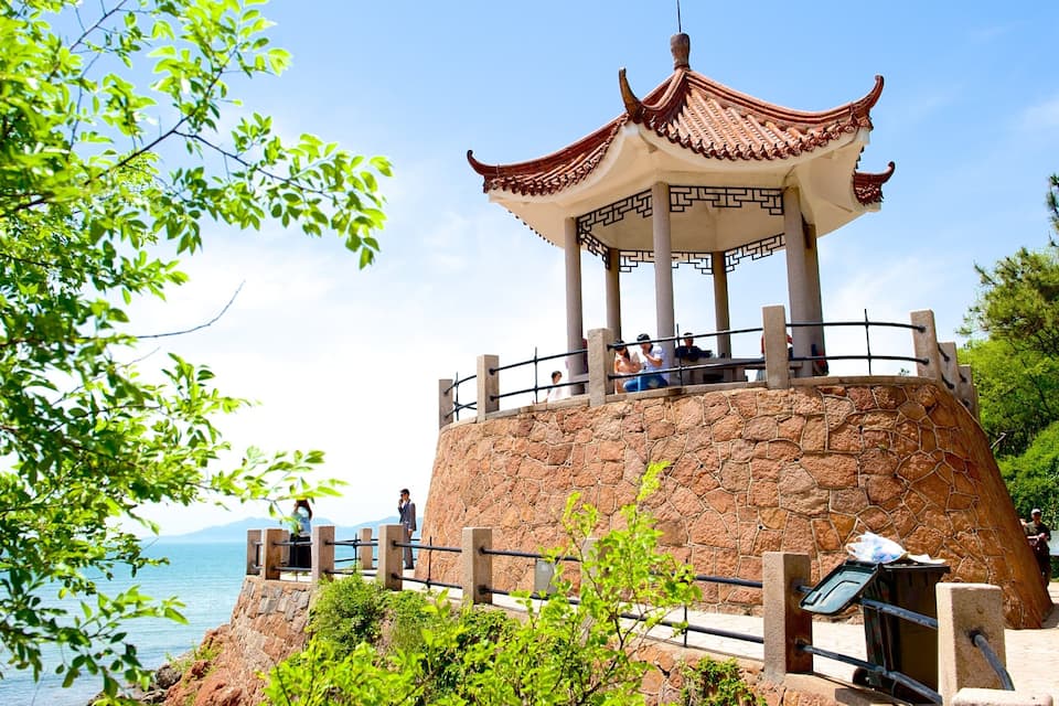 A traditional Chinese pavilion on a rocky outcrop with a view of the sea.