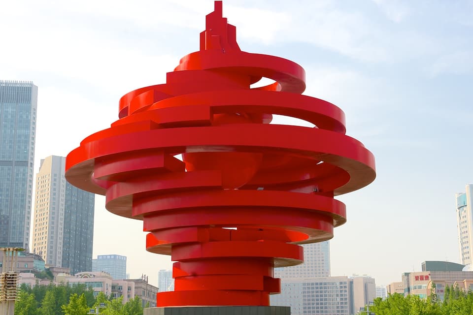 A red spiral sculpture in an urban setting with modern buildings in the background.