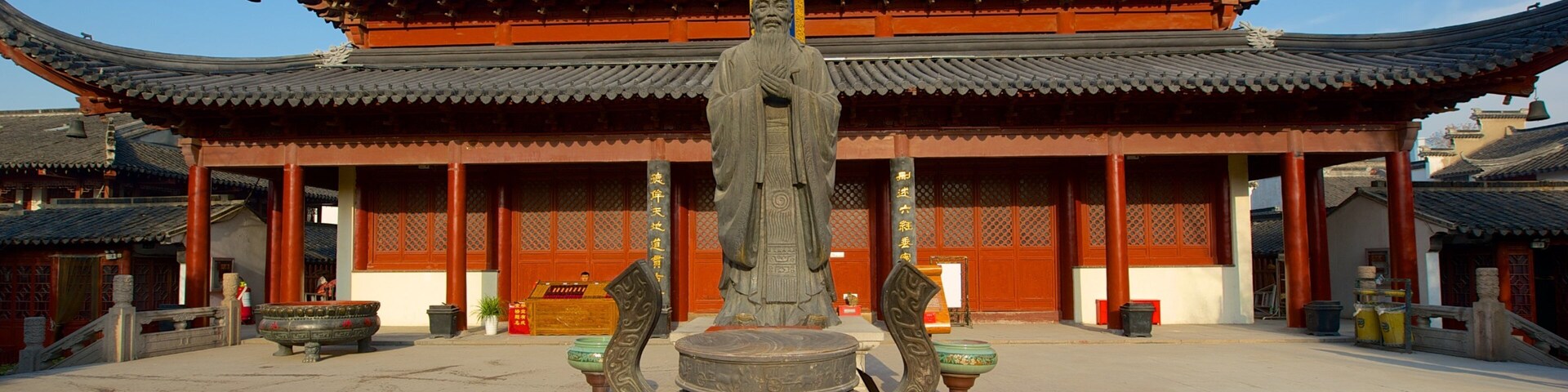 Um edifício tradicional chinês com telhado curvo e decorações elaboradas. Em frente ao edifício, há uma grande estátua de pedra e um altar de pedra.