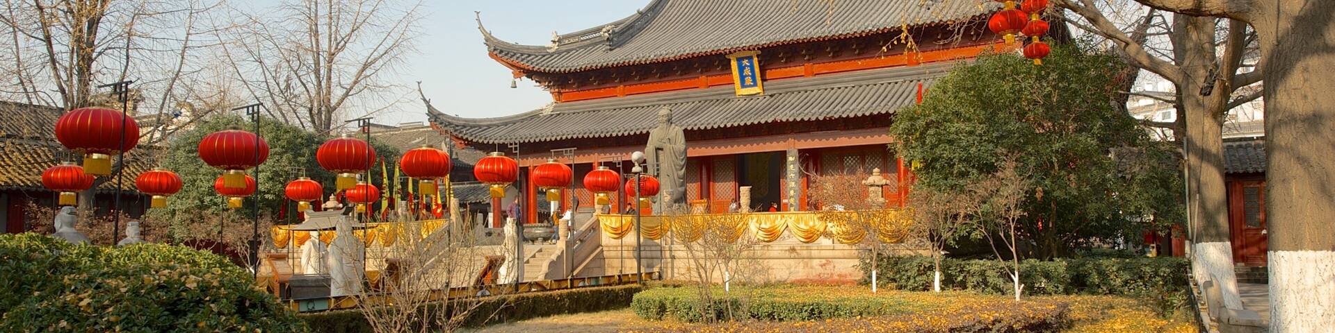 A traditional Chinese building with red lanterns, autumn leaves, and a statue.