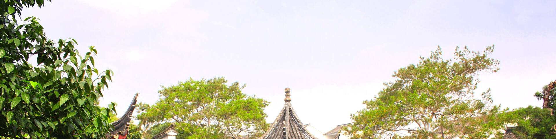A traditional Chinese pavilion over a pond with a stone pathway and lush greenery.