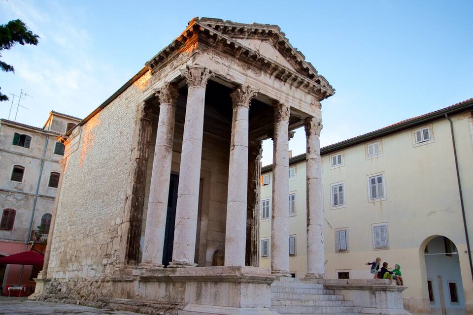 Un antiguo templo romano con columnas y frontón, rodeado de edificios modernos.