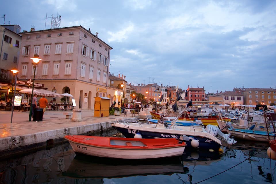 Um porto com barcos atracados, um calçadão à beira-mar e edifícios históricos.