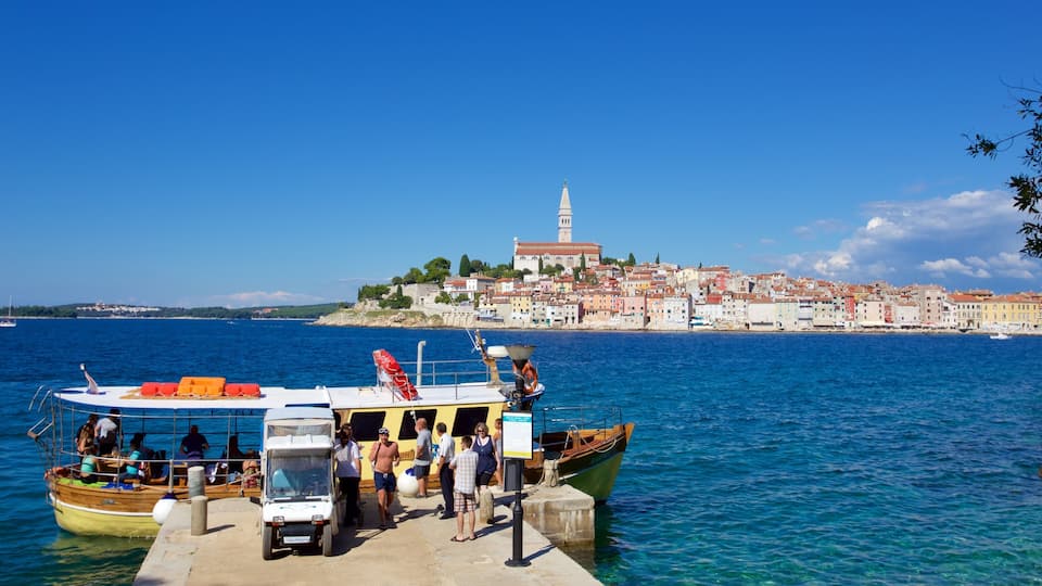 A coastal town with a prominent church and tower, boats docked at a pier, and clear blue waters.
