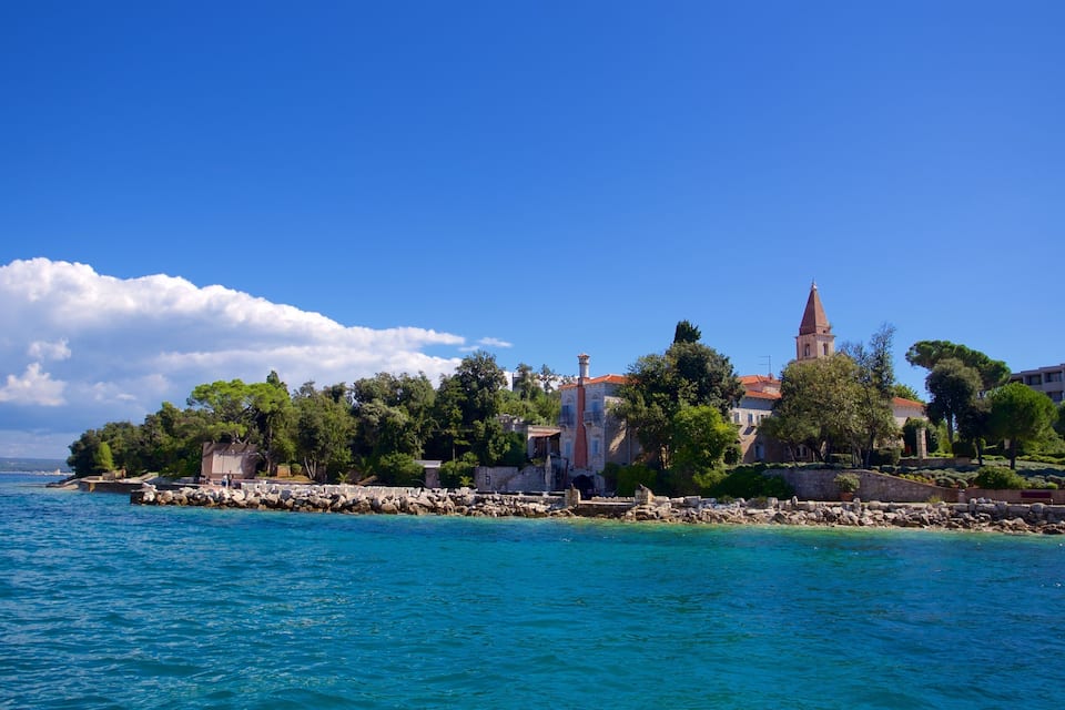 Uma vila costeira com uma igreja e torre imponentes, cercada por árvores e um litoral rochoso.