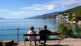 A couple sitting on a bench overlooking a calm lake with a mountain in the background.