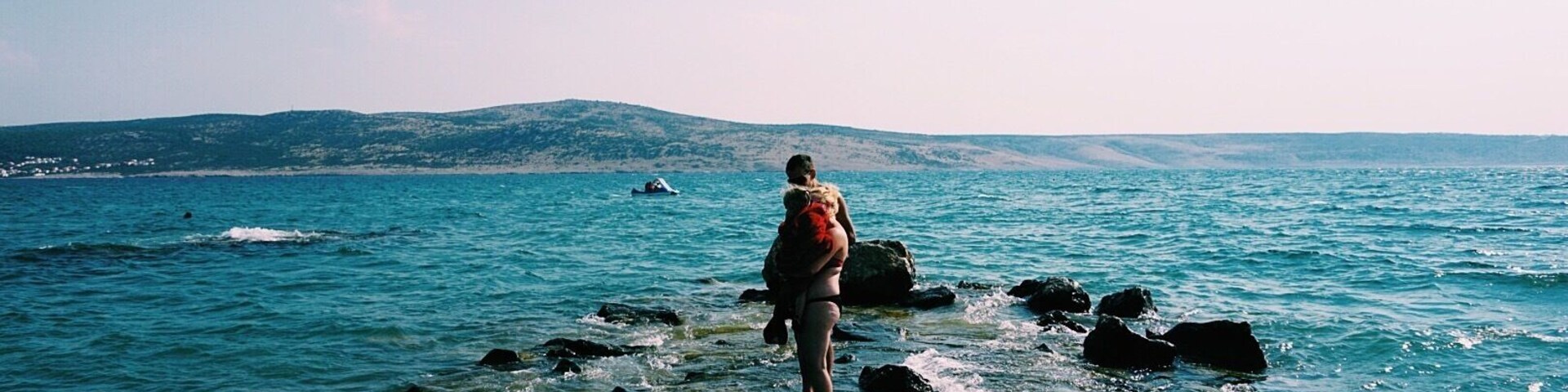 Eine Person geht an einer felsigen Küste entlang, im Hintergrund das Meer.