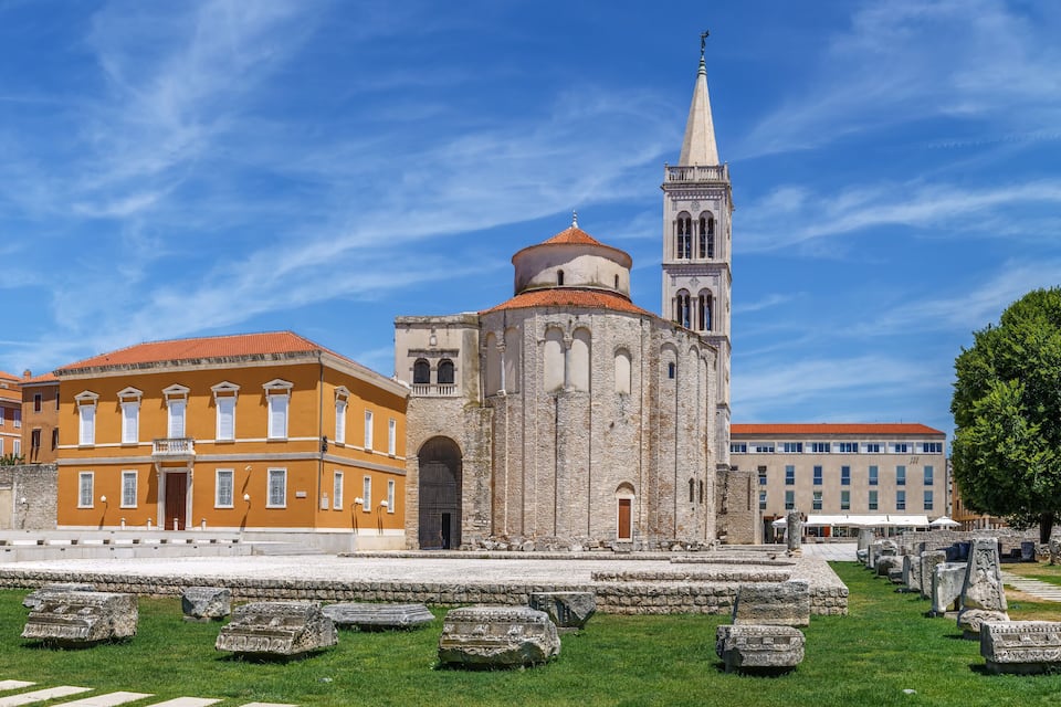 A historic church with a tall bell tower, a red-roofed building, and a cemetery with ancient gravestones.