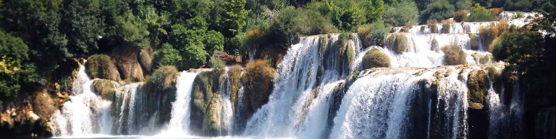A waterfall cascading into a clear blue pool surrounded by lush greenery.