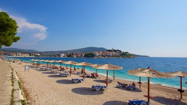 A beach with rows of sun loungers and umbrellas, a clear blue sea, and a town in the background.