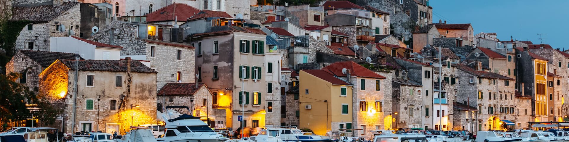 A coastal town with historic stone buildings, a prominent castle on a hill, and a marina with boats.